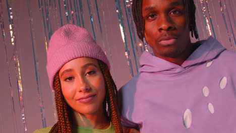 Studio-Portrait-Shot-Of-Young-Gen-Z-Couple-Standing-In-Front-Of-Tinsel-Curtain-Against-Pink-Background-1